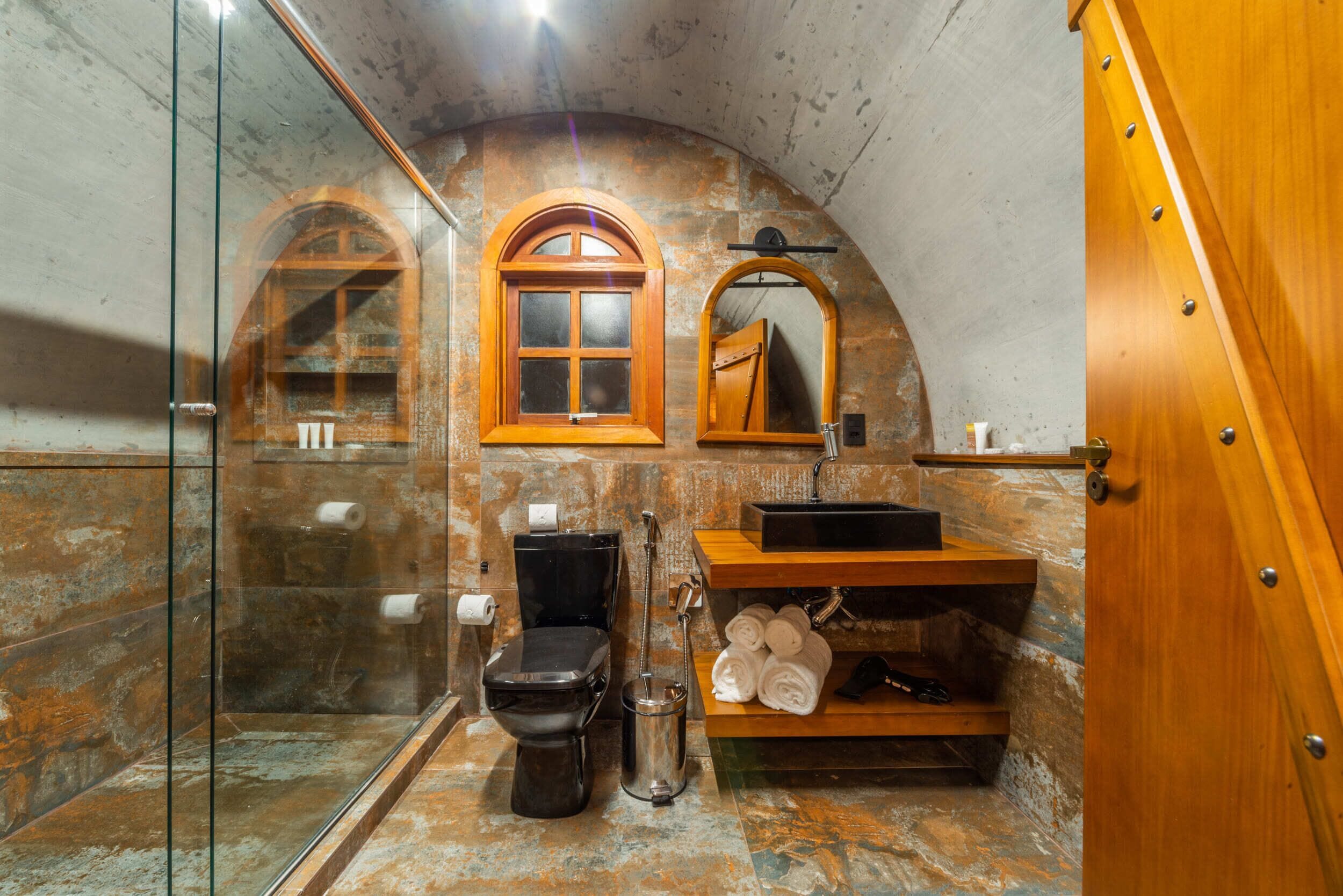 Un baño con cabina de ducha de vidrio, inodoro negro, tocador de madera con lavamanos y espejo.