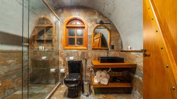 Un baño con cabina de ducha de vidrio, inodoro negro, tocador de madera con lavamanos y espejo.
