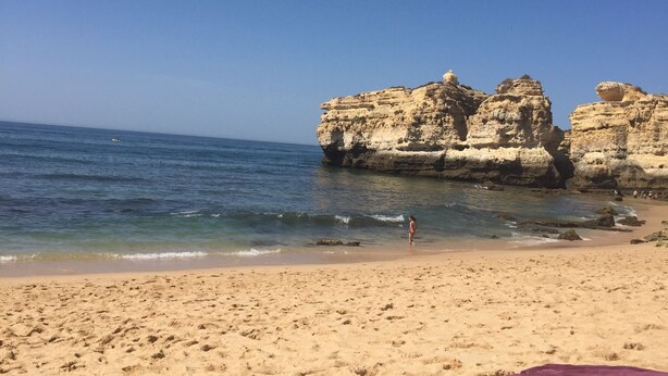 Una spiaggia con cielo sereno, formazioni rocciose e un litorale sabbioso.
