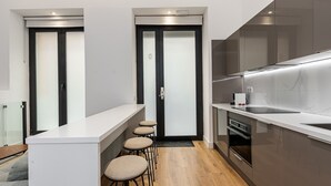 Una cucina moderna con piano di lavoro bianco, mobili scuri e forno integrato. Sotto il piano ci sono tre sgabelli e una porta con vetri acidati.