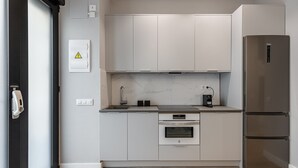 Une cuisine moderne avec des meubles blancs, un réfrigérateur en acier inoxydable, un four et une machine à café posée sur le plan de travail.