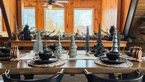 A wooden dining area with a high ceiling, a ceiling fan, and a view of autumn trees through large windows.