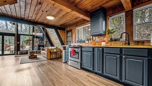 A spacious kitchen with dark cabinets, a wooden ceiling, and large windows offering a view of the outdoors.