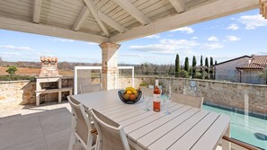 Une terrasse extérieure avec une table, des chaises, un barbecue et une vue sur la piscine.