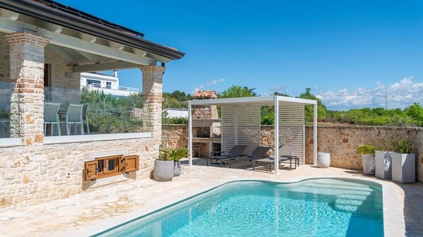 Un bâtiment en pierre doté d’une piscine, d’un espace extérieur aménagé et d’une zone couverte.