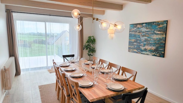 A dining area with a wooden table set for six, a hanging light fixture, and a painting on the wall.