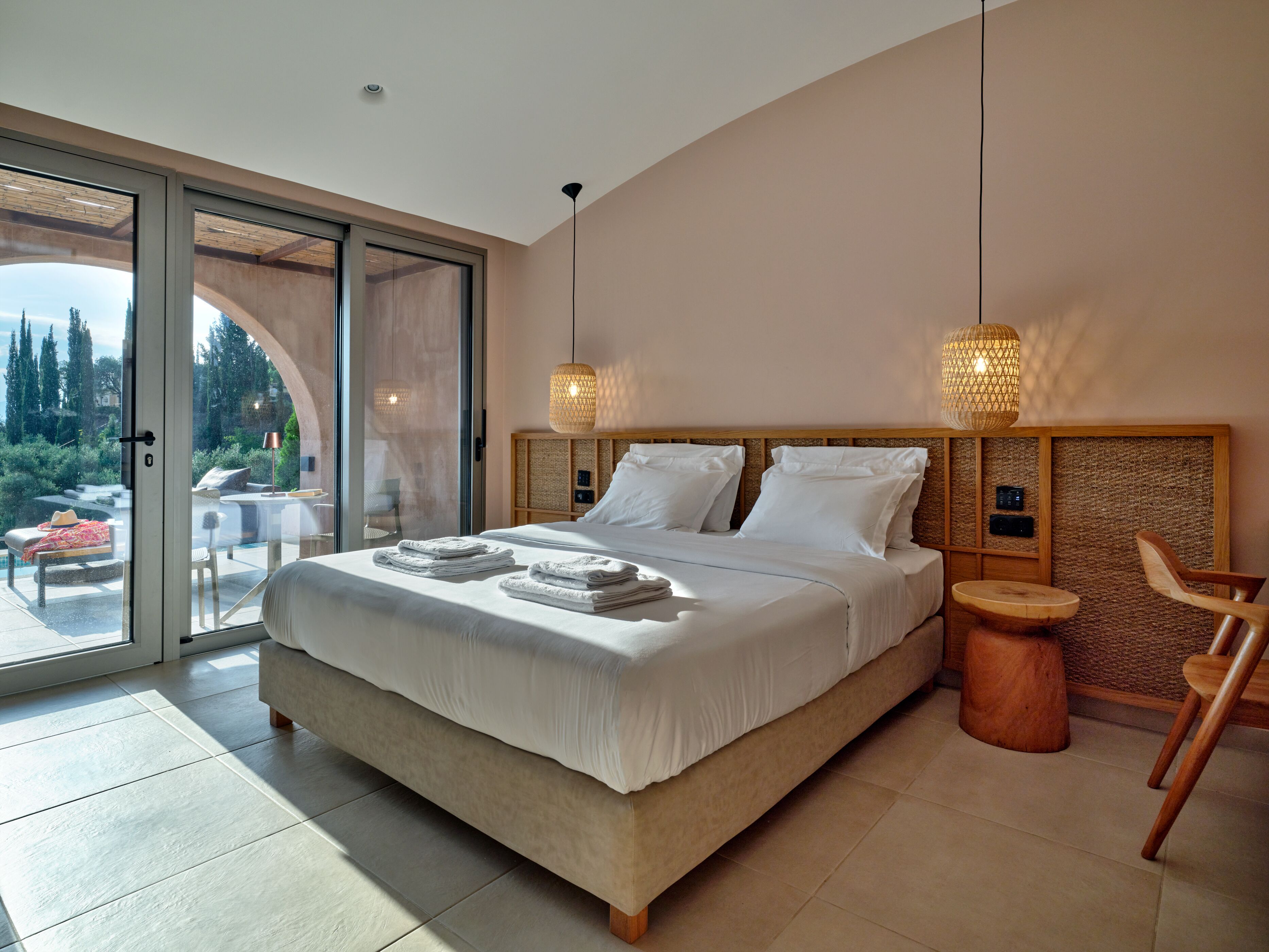 A spacious bedroom with a large bed, a wooden headboard, and a view of a garden through a sliding glass door.