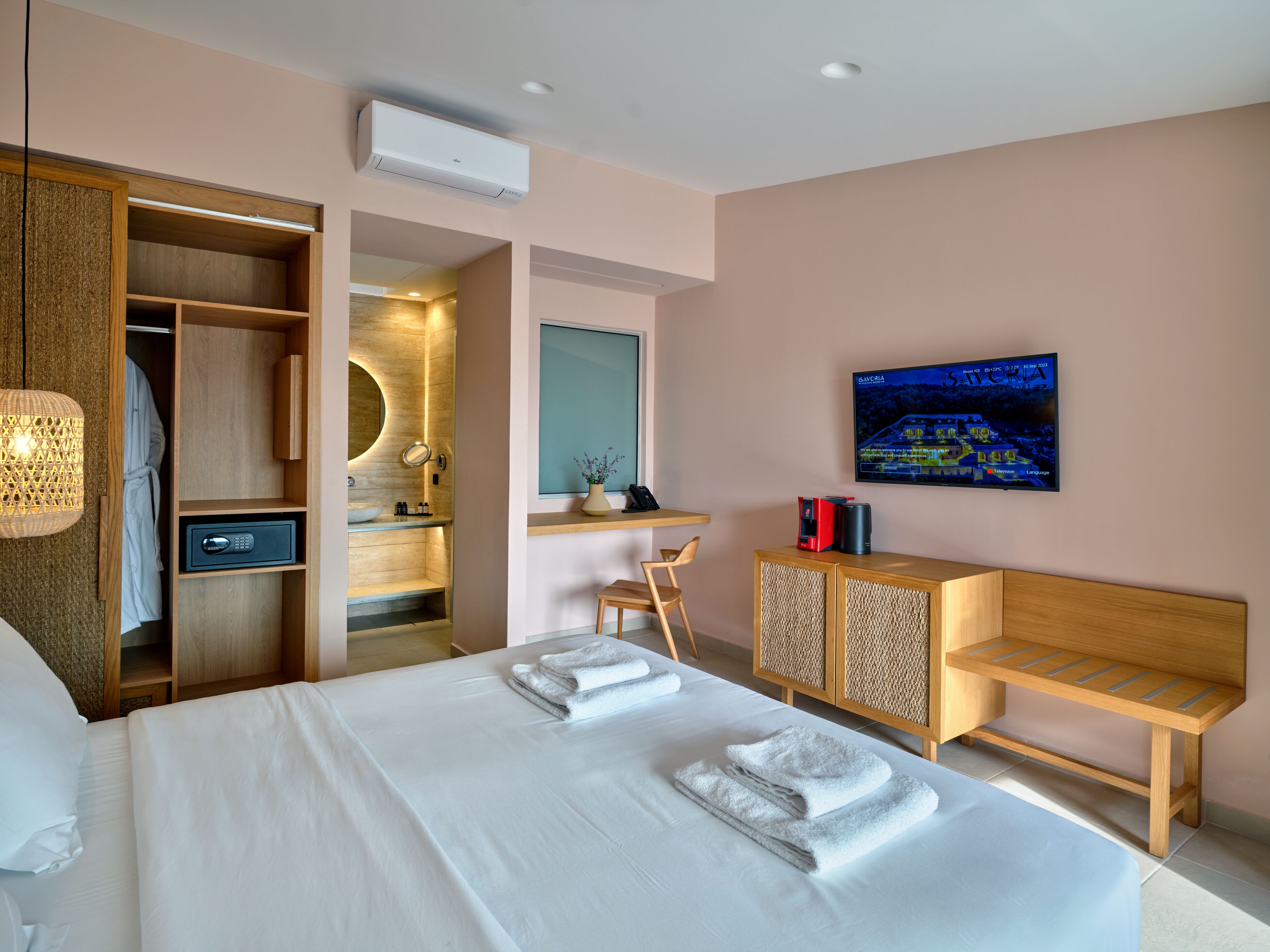 Een moderne hotelkamer met een groot bed, een inloopkast, een badkamer met wastafel en een aan de muur bevestigde televisie.
