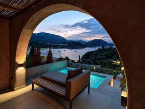 A balcony with a pool, a sofa, and a view of a lake and mountains. - Isavoria Resort (Parga)