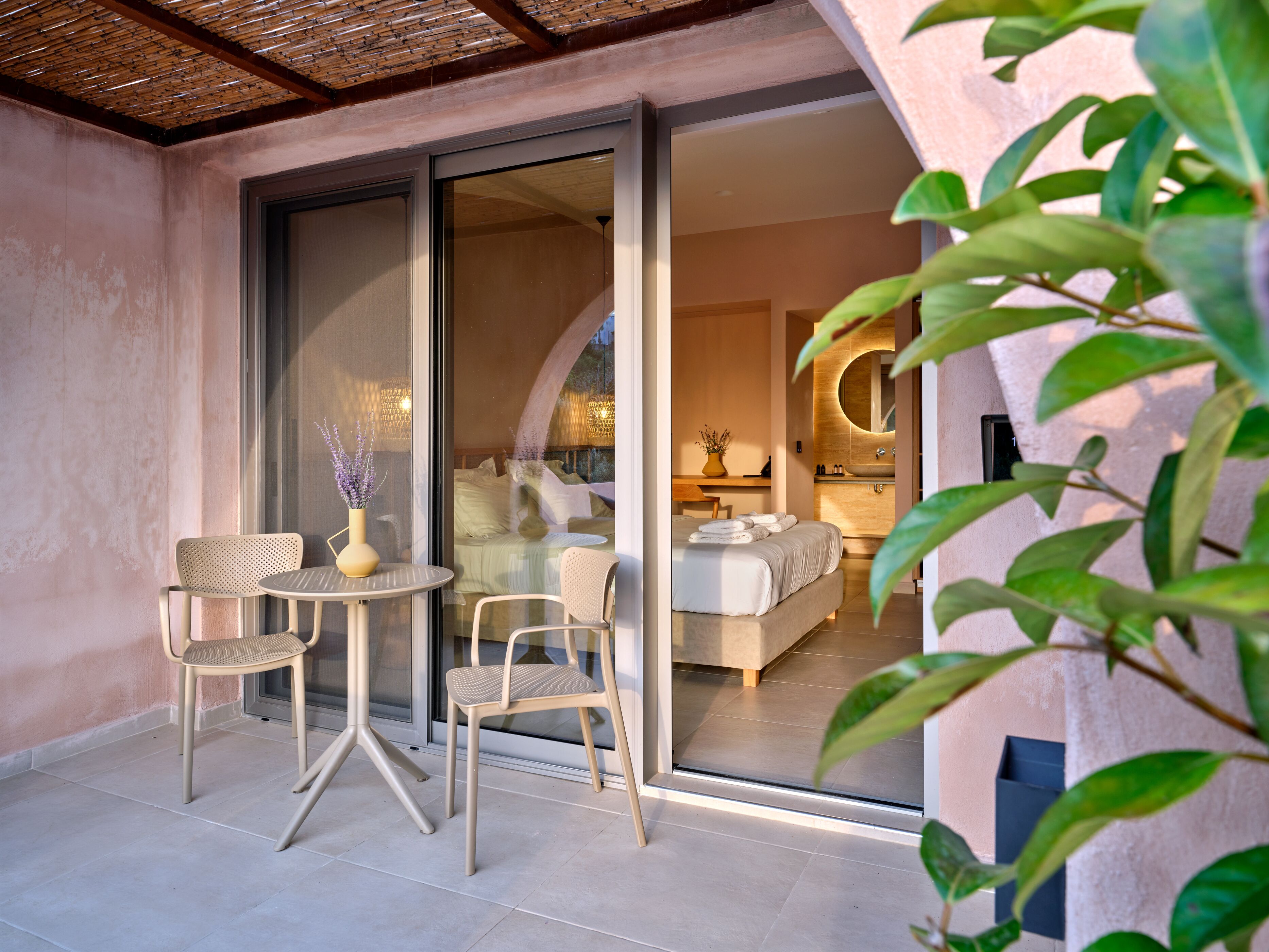 Une chambre d’hôtel moderne dotée d’une grande porte-fenêtre coulissante donnant sur un balcon avec deux chaises et une table.