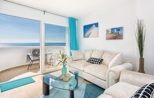 Una sala de estar moderna con una mesa de centro de vidrio, un sofá color beige y vista al mar a través de ventanas amplias.