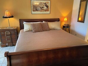 A neatly made bed with a wooden headboard, two bedside lamps, a decorative chest of drawers, and a framed picture on the wall. - Jim Miller's Safari Premium Theme Condo (Lutz)