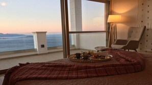 A bedroom with a large window overlooking a body of water, a bed with a red blanket, a chair, and a tray with food and drinks. - Endless View Villa close to the beach (Agios Nikolaos)