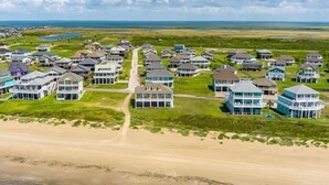 Uma área residencial à beira-mar com casas que apresentam grandes janelas e varandas, uma praia arenosa e uma vista clara do oceano.