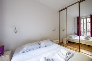 A hotel room with a large bed, a bedside table, a mirror, and a view through a glass door.