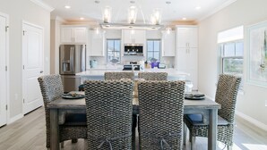 Una cocina moderna con armarios blancos, un refrigerador de acero inoxidable y un comedor con sillas de mimbre y una mesa de madera.