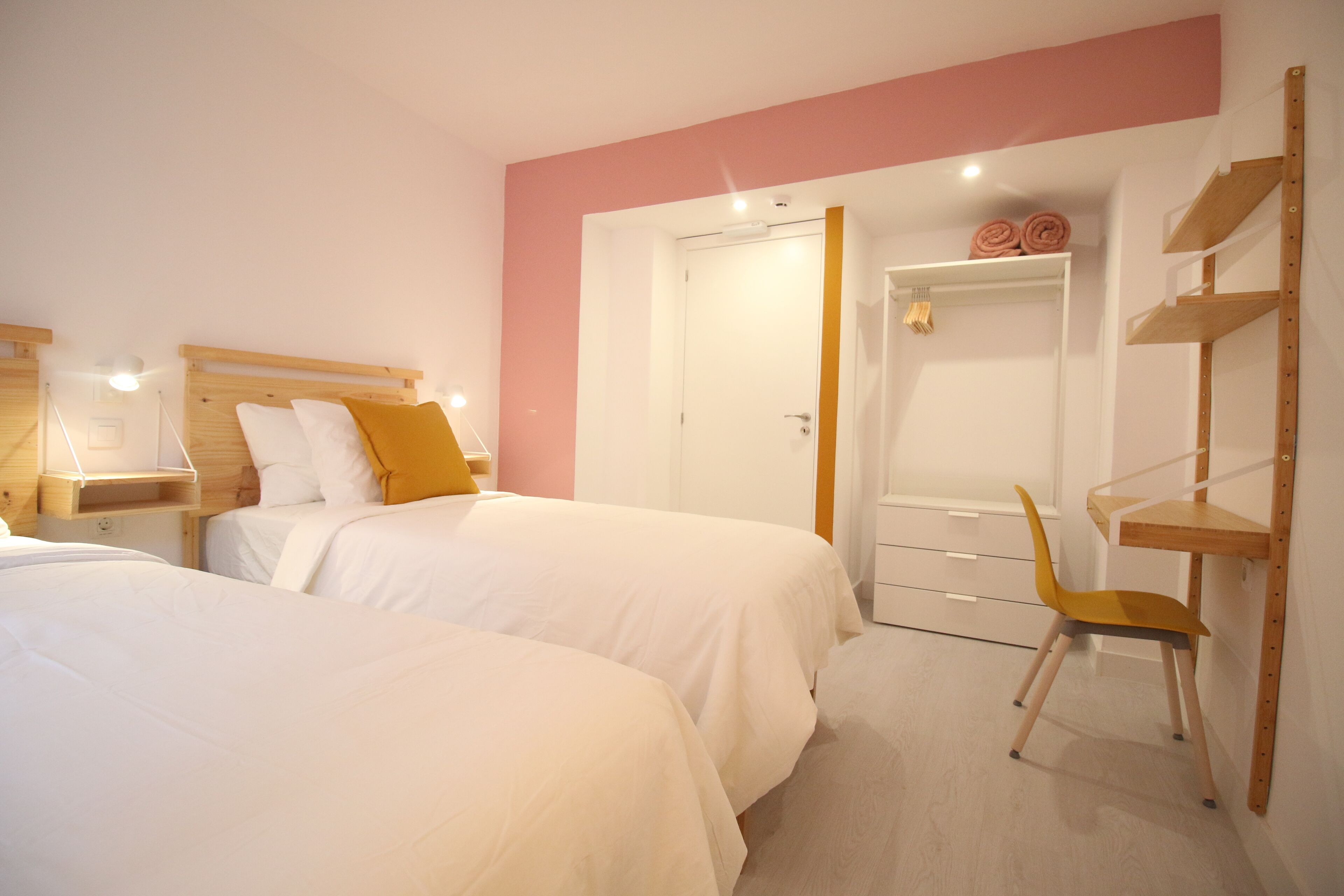 A bedroom with two beds, a wooden chair, a wardrobe, and a desk.