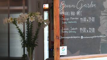 Un espace d’accueil avec un comptoir en bois, un vase rempli de fleurs et un panneau indiquant les heures d’ouverture du bar.