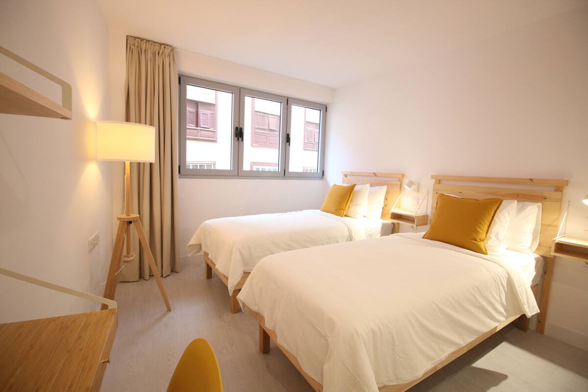 Ein Hotelzimmer mit zwei Betten, einem Schreibtisch, einem Stuhl und einem Fenster mit Vorhängen.