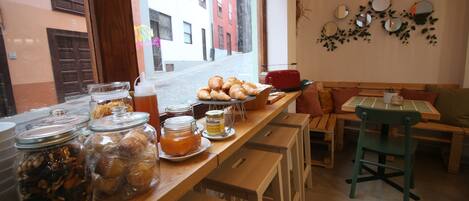 A café with a wooden counter displaying pastries, jars of spreads, and a view of a street through the window.