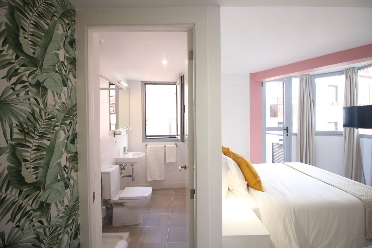 Ein Hotelzimmer mit Bett, Badezimmer mit Toilette und Waschbecken sowie Balkon mit Vorhängen.