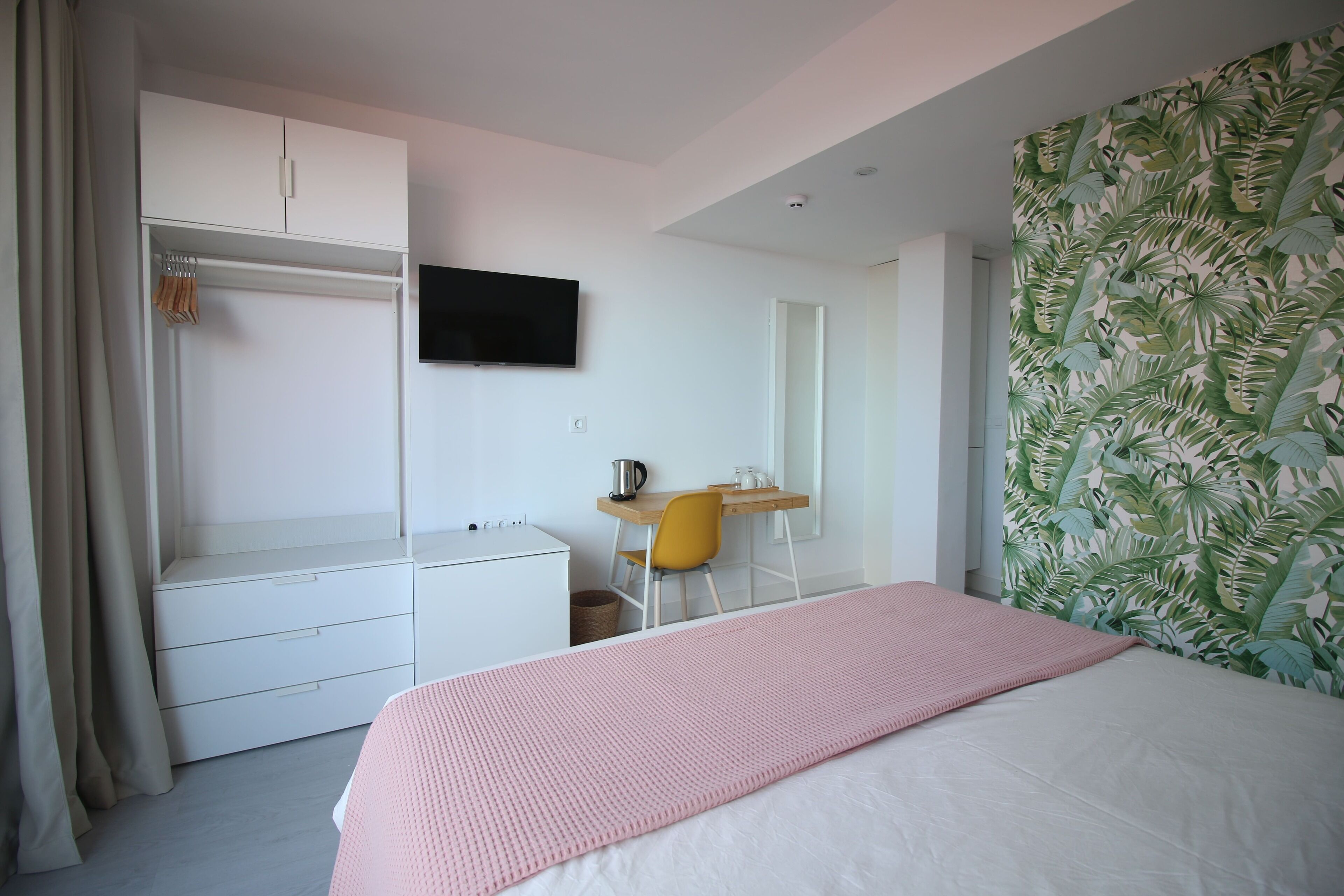 A bedroom with a bed, a desk, a chair, a wardrobe, and a television on the wall.