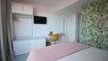 A bedroom with a bed, a desk, a chair, a wardrobe, and a television on the wall.
