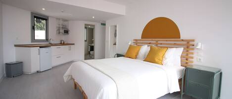 A modern bedroom with a large bed, a bedside table, and a built-in kitchen area.
