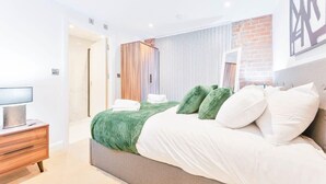 A modern bedroom with a large bed, a wooden dresser, and a television on a side table. - Cosy 1 Bedroom Apartment in Burton-on-Trent (Burton upon Trent)