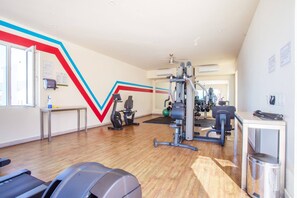 Et fitnessrum med løbebånd, styrketræningsudstyr og et spejl.