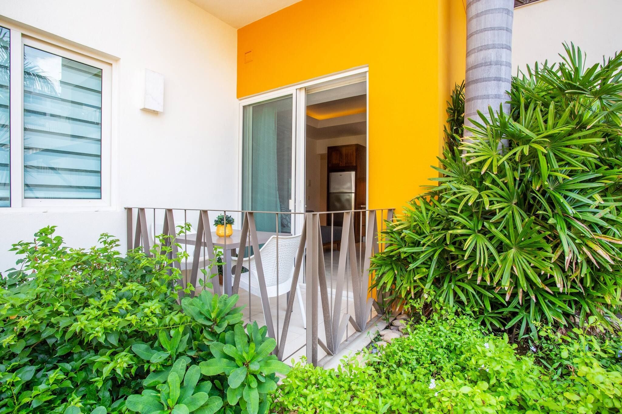 Ein modernes Apartment mit Balkon, einer Schiebetür aus Glas und einem kleinen Gartenbereich mit verschiedenen Pflanzen.