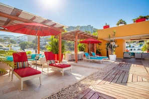An outdoor lounge area with red umbrellas, lounge chairs, and potted plants.