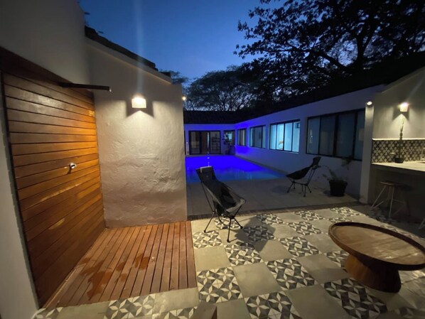 A modern outdoor patio with a pool, wooden deck, and patterned tiles.
