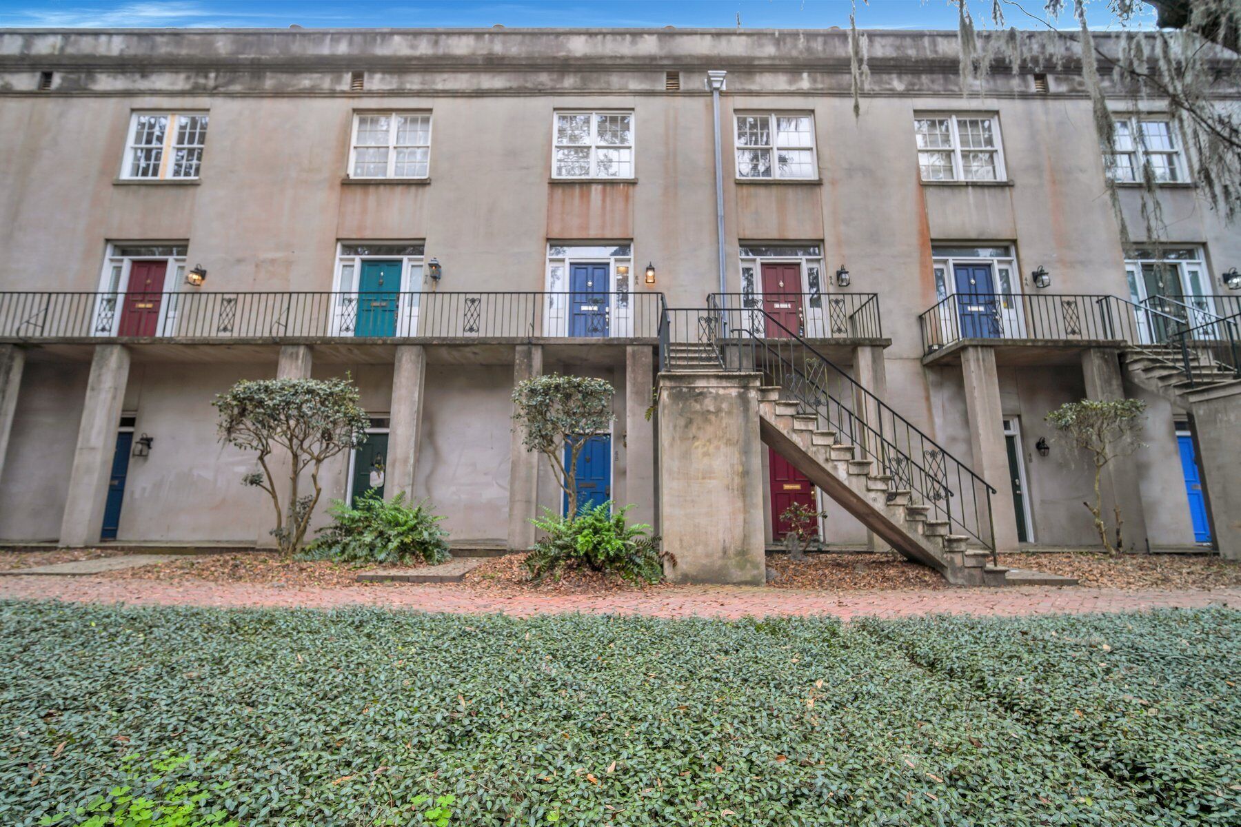 Una hilera de casas adosadas con una escalera central, pequeños árboles y un camino pavimentado.