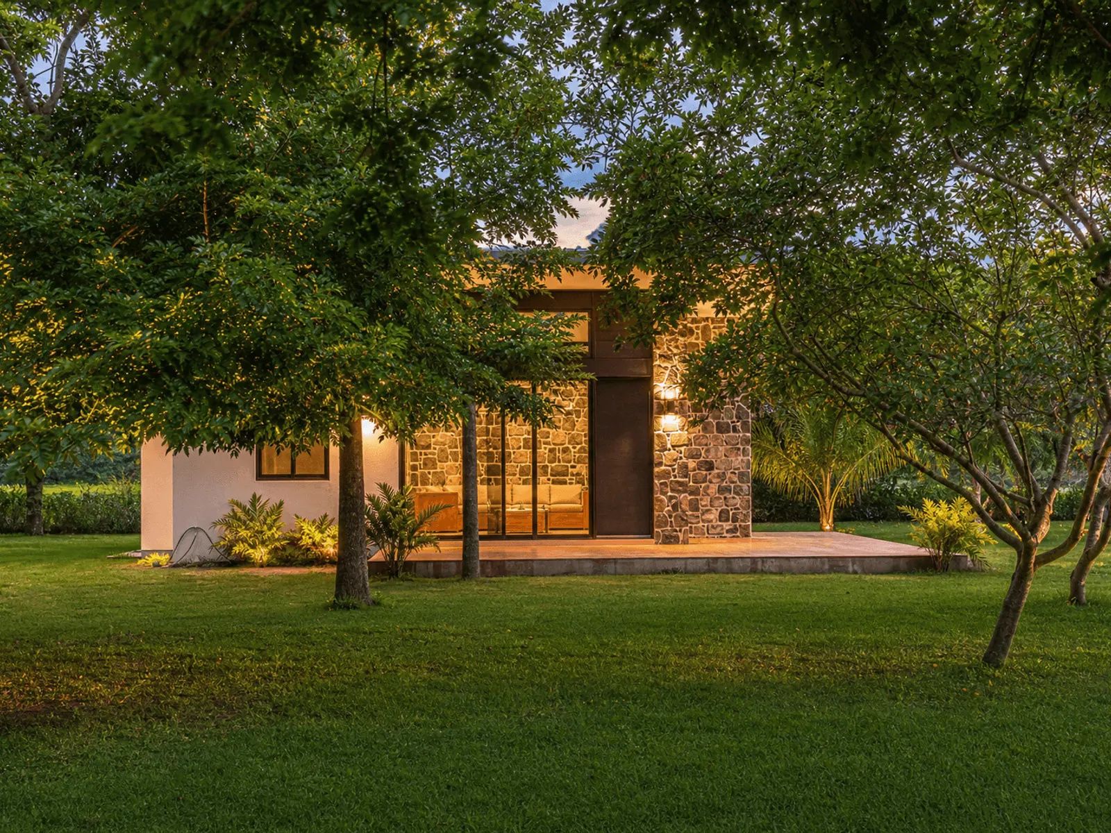 Una casa moderna con fachada de piedra, césped cuidado y un árbol grande al frente.