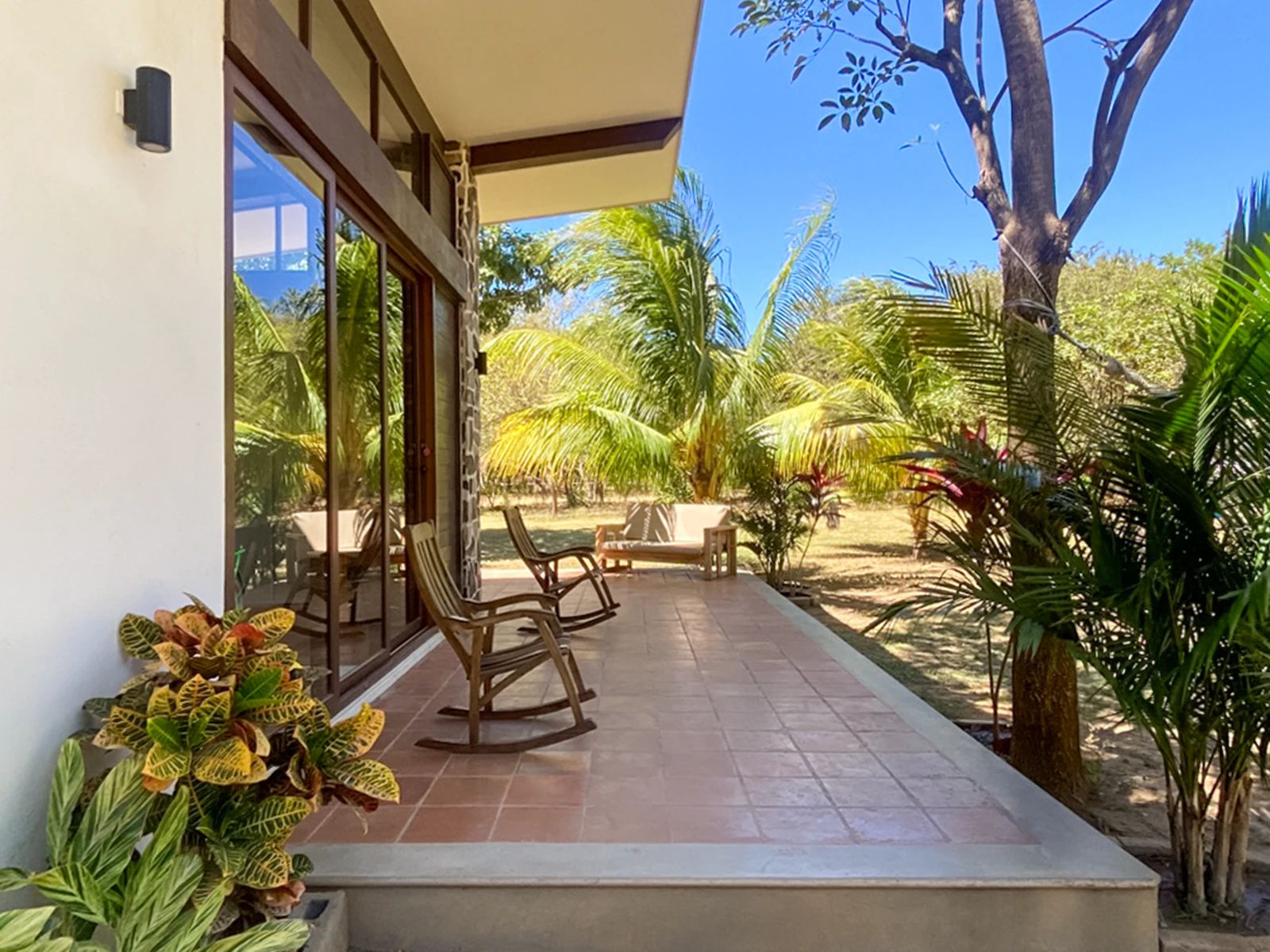 Un espace extérieur abrité, aménagé avec des chaises et une table, et entouré de plantes et d’arbres tropicaux.
