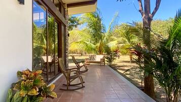 Un espace extérieur abrité, aménagé avec des chaises et une table, et entouré de plantes et d’arbres tropicaux.