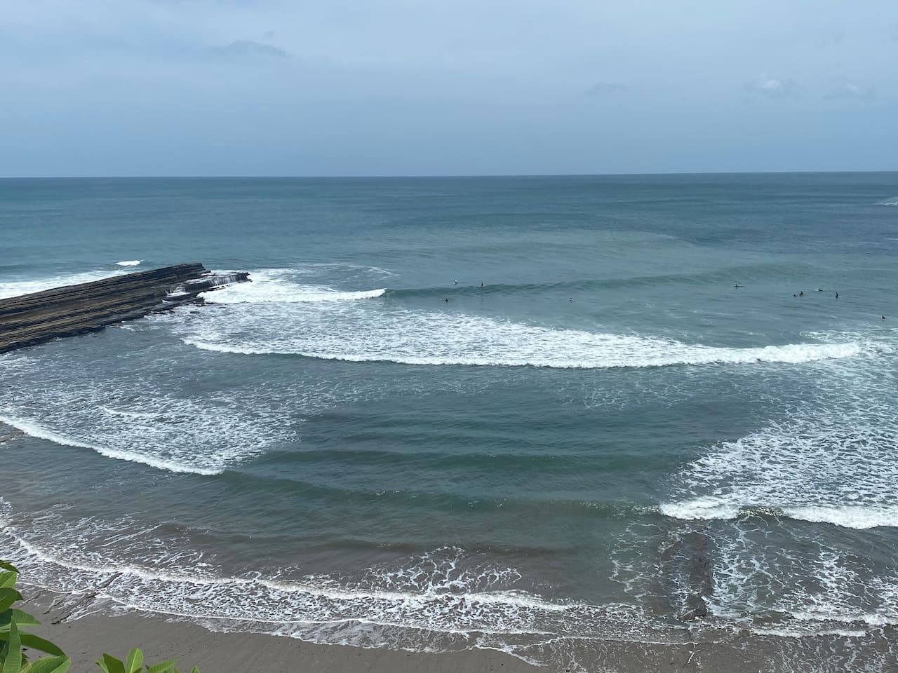 A coastal beach with waves, a wooden jetty, and a clear sky.