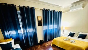 A hotel room with two beds, wooden flooring, and a window with blue curtains. - DMCharme (Ponta Delgada)