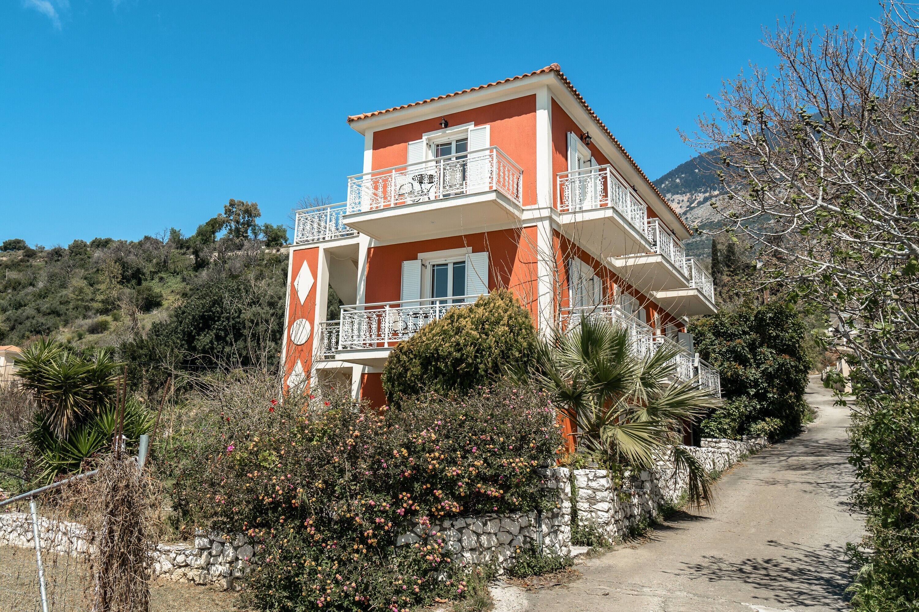 A two-story building with balconies, surrounded by vegetation and a clear sky.