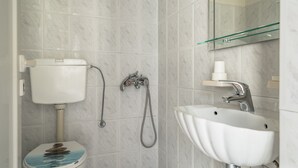 A bathroom with a toilet, shower, sink, and a glass shelf above the sink. - Room “Angela Partial Sea View 8” with Sea View, Wi-Fi and Air Conditioning (kefalonia)