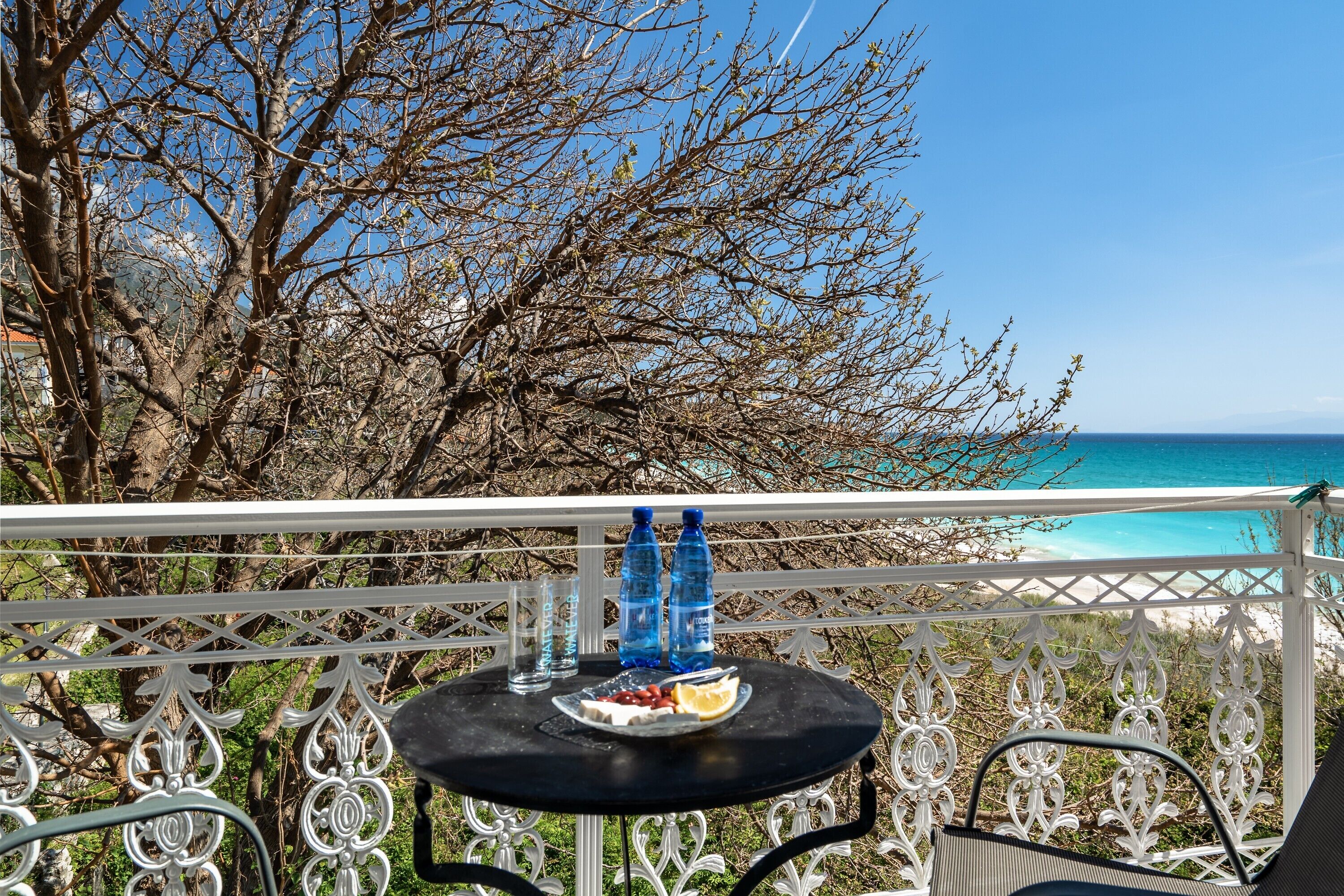 Ein Balkon mit Tisch, zwei Wasserflaschen, einem Teller mit Essen und einem Stuhl.