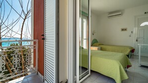 A room with a balcony, a bed with a green bedspread, a white door, and a view of the sea. - Room “Angela sea view 7” with Sea View, Wi-Fi, and Air Conditioning (kefalonia)