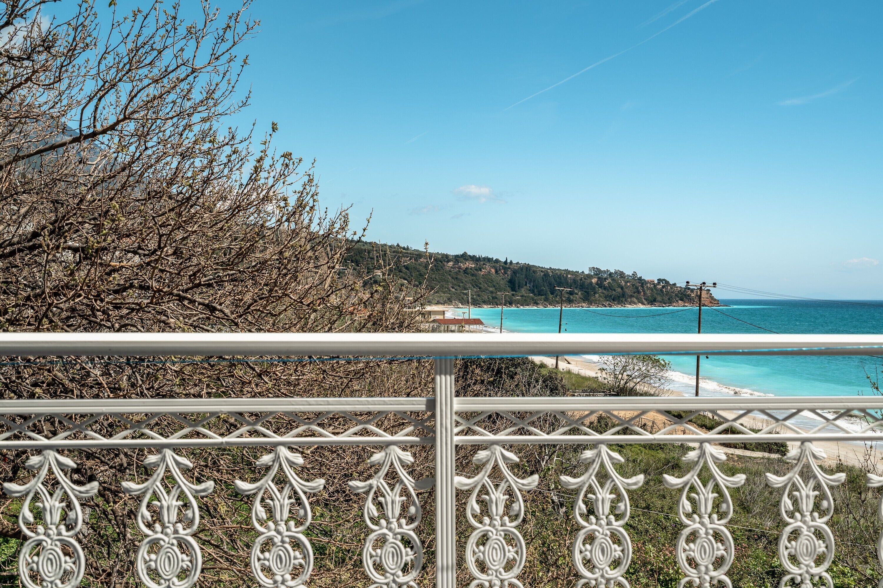 Un balcon doté d’une rambarde en métal, donnant sur un paysage côtier avec des arbres et une plage.