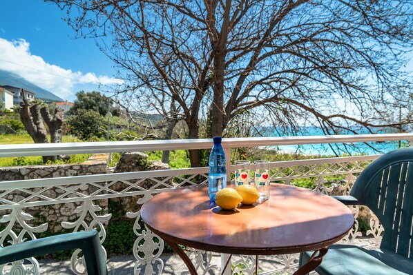 A round wooden table with two lemons and a water bottle, a green chair, and a white railing with a view of a tree and a body of water.