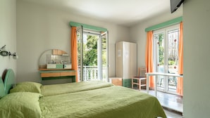 A room with two beds, a desk, a chair, a mirror, a wardrobe, and a balcony with orange curtains. - Room “Angela partial sea view 6” with sea view, Wi-Fi, and air conditioning (kefalonia)