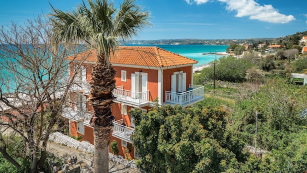 A coastal building with balconies, a palm tree, and a view of the sea. - Room “Angela partial sea view 6” with sea view, Wi-Fi, and air conditioning (kefalonia)