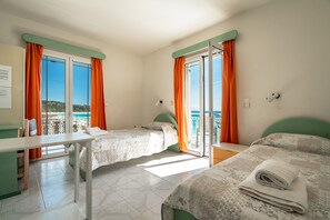 A hotel room with two beds, a desk, and a balcony with orange curtains. - Room "Angela sea view 4" with sea view, Wi-Fi, and air conditioning (kefalonia)