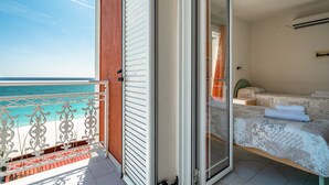 A balcony with a view of the sea, a bed with a patterned bedspread, and a sliding glass door leading to a room with a bed and a nightstand. - Room "Angela sea view 4" with sea view, Wi-Fi, and air conditioning (kefalonia)