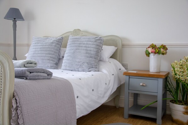 A neatly made bed with pillows and a bedside table with a lamp and a vase of flowers. - Hewas Water House with Pool, Hot Tub & Games Room (St Austell)